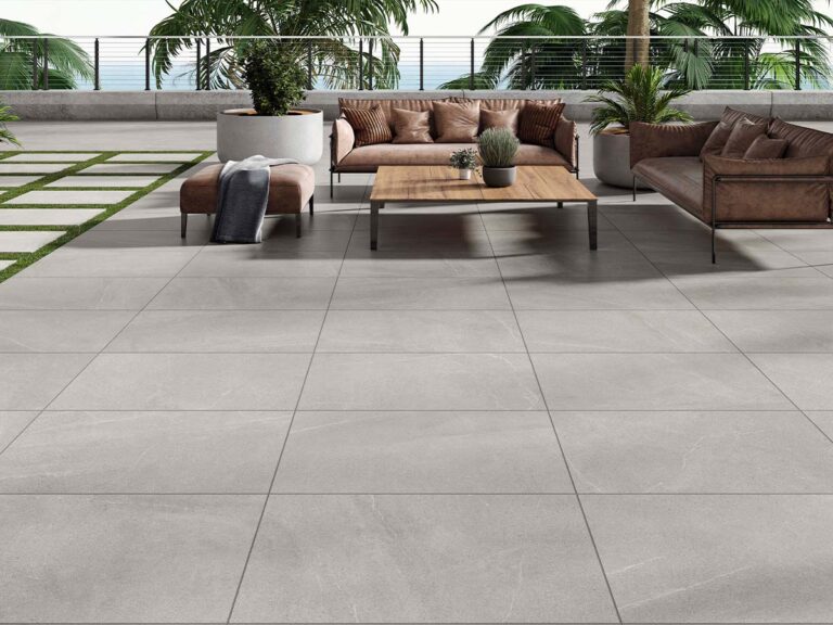 baldosa exterior antideslizante bellevue grey en una amplia terraza con vistas al mar, equipada con sofás de cuero marrón, una mesa de centro de madera y palmeras al fondo