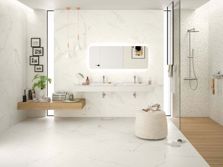 Ambiente de un baño moderno blanco con el suelo y las paredes revestidos con baldosas Lancelot Gold de imitación mármol, en combinación con un mosaico en la pared y un suelo de madera en la ducha.
