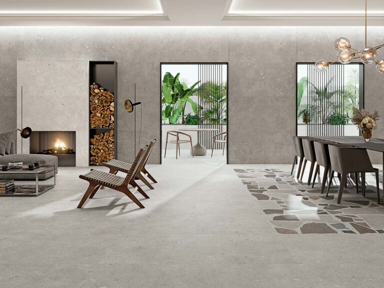 Ambiente de salón de lujo con paredes y suelo revestidos con la baldosa Glamstone White, que crea una base luminosa de imitación piedra para una zona de comedor con una alfombra de mosaico decorativo.