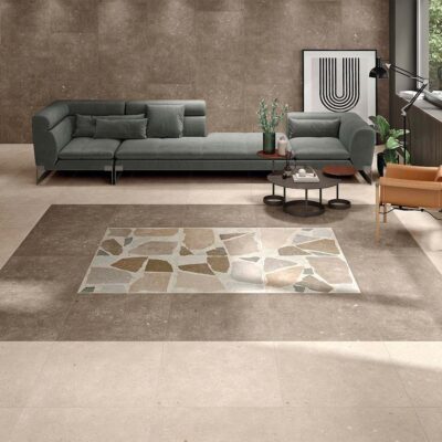 Suelo de un salón moderno con baldosas de porcelánico Glamstone Beige efecto piedra, que sirve de base para una alfombra decorativa hecha con baldosas más oscuras y un mosaico central.