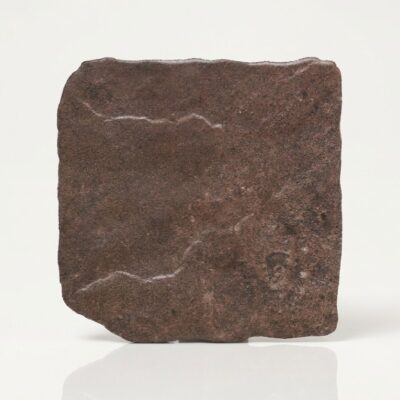 Azulejo porcelánico imitación piedra rodeno. Superficie rugosa marrón rojiza con bordes irregulares.