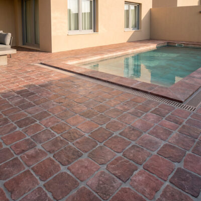 Patio exterior con suelo porcelánico efecto piedra rodeno rodeando una piscina.