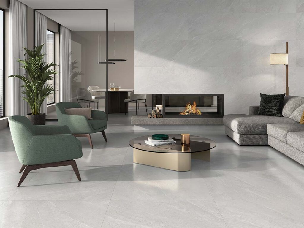 Salón moderno con suelo y pared de chimenea revestidos con azulejo Sakhir Soft Grey brillante, efecto mármol en gris claro con vetas blancas