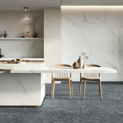 Pared de cocina moderna revestida con el azulejo Lumiere White, cuyo efecto mármol blanco se extiende a la isla y mesa de comedor, creando un fuerte contraste con el suelo oscuro.