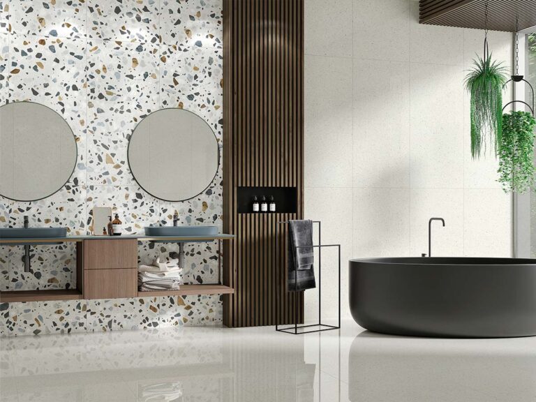 Azulejo de pared Crisp XL White, con efecto terrazo sobre base blanca y fragmentos multicolores (negro, gris, ocre), instalado como revestimiento en la pared de una moderna cocina-comedor, contrastando con el suelo de terrazo oscuro.