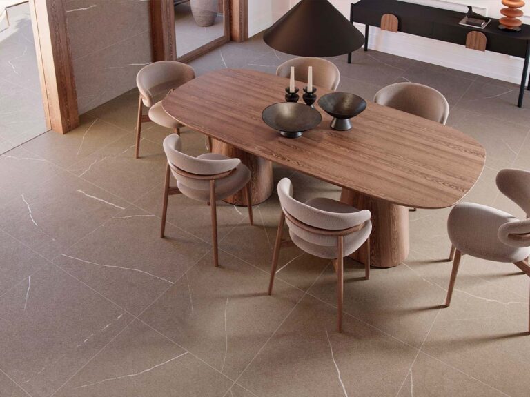 Pavimento efecto piedra Origins Natural, en un cálido tono tierra con vetas blancas, ambientado en un comedor moderno con mesa de madera.