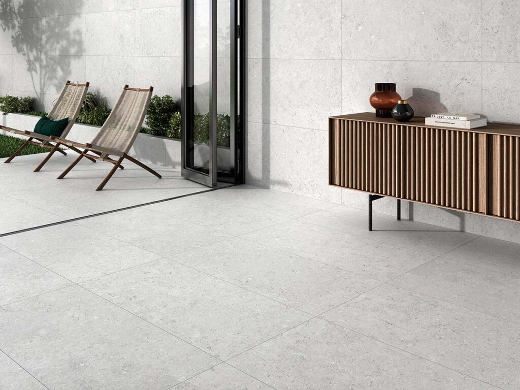 Suelo y pared revestidos con porcelánico Caliope White, efecto piedra en tono blanco con sutiles inclusiones, en un espacio que conecta interior y exterior.