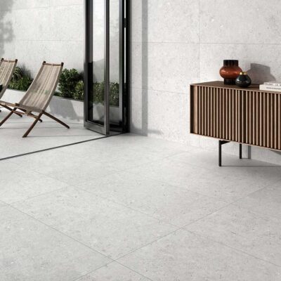 Suelo y pared revestidos con porcelánico Caliope White, efecto piedra en tono blanco con sutiles inclusiones, en un espacio que conecta interior y exterior.