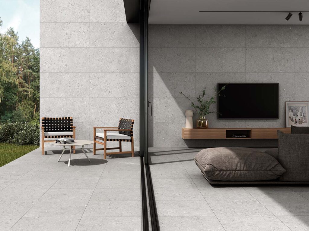 Ambiente de salón y terraza con suelo y pared revestidos con porcelánico Caliope Pearl, mostrando la continuidad del efecto piedra gris del interior al exterior.