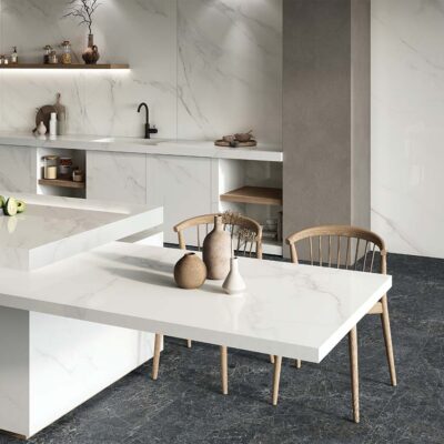 Cocina de lujo con paredes, salpicadero y encimeras revestidas con el porcelánico Lumiere White, que crea un efecto de mármol blanco en contraste con el suelo oscuro.