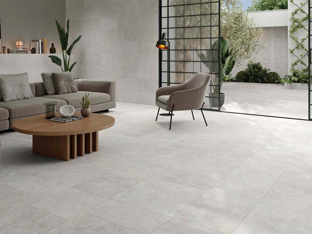 Ambiente de un salón moderno con el porcelánico interior Premiere Grey revistiendo el suelo y la pared, mostrando una superficie continua de efecto piedra gris que se prolonga hasta la terraza.