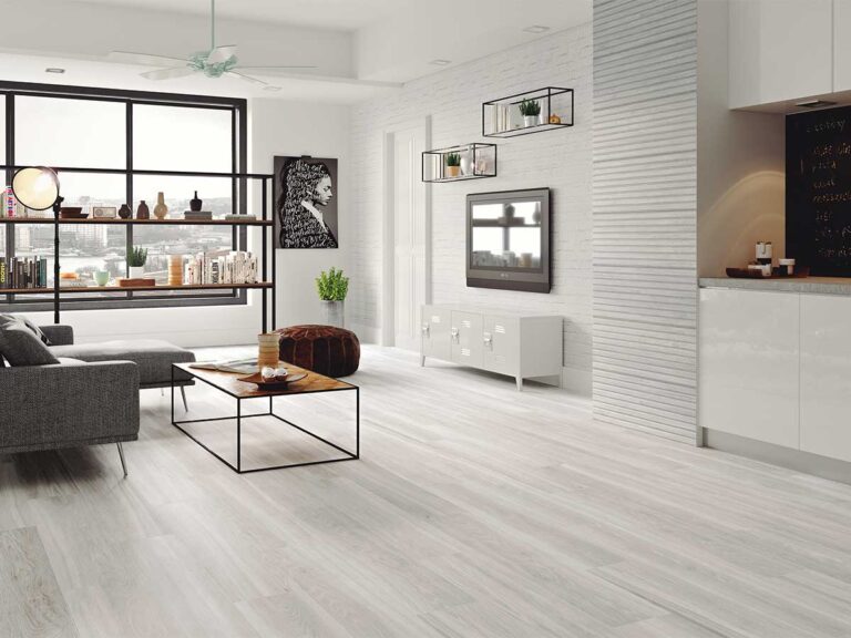 suelo cerámico efecto madera kimberley blanco en un salón moderno con sofás grises, estantería metálica de estilo industrial y pared de ladrillo visto blanco
