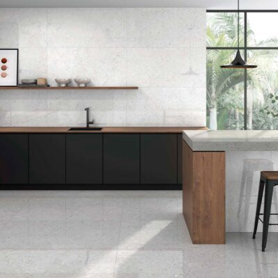 Suelo de cocina con baldosas Caliope White, imitación piedra en tono blanco con sutiles inclusiones, en una cocina moderna con paredes a juego, muebles negros y encimeras de madera.