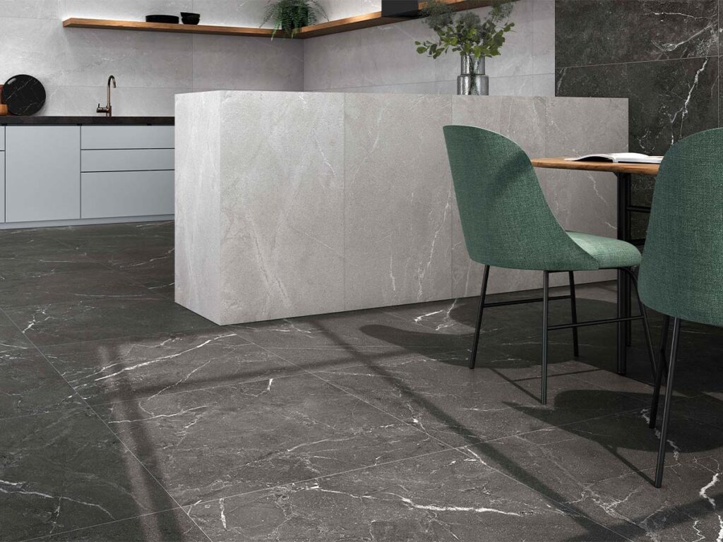 Suelo de cocina con baldosas Malek Black, efecto piedra oscura con vetas blancas, en una cocina moderna con isla y paredes revestidas en tonos grises claros a contraste.