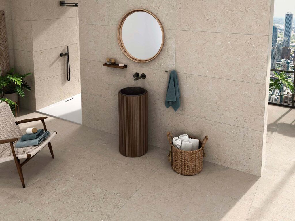 Baño moderno con suelo y paredes revestidos con baldosas Caliope Beige, efecto piedra en tono beige claro con sutiles inclusiones, y vistas a la ciudad.