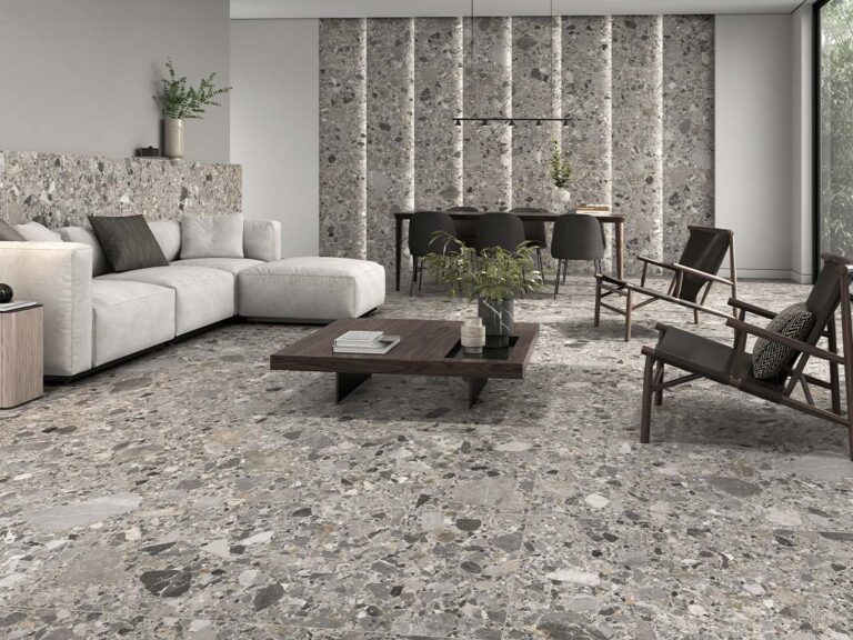 Suelo porcelánico para interior con efecto piedra y detalles de incrustaciones (Inlay) en tonos naturales, ambientado en un salón-comedor moderno con pared parcialmente revestida a juego.