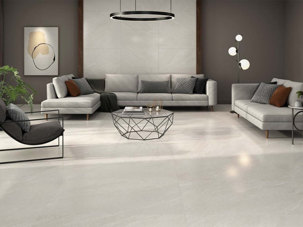 Suelo porcelánico interior Sakhir Soft Ivory, imitación piedra en un cálido tono marfil con sutiles vetas blancas, utilizado en el pavimento y como pared de acento en un elegante salón moderno.