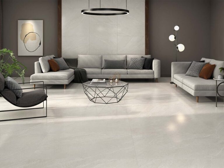 Suelo porcelánico interior Sakhir Soft Ivory, imitación piedra en un cálido tono marfil con sutiles vetas blancas, utilizado en el pavimento y como pared de acento en un elegante salón moderno.