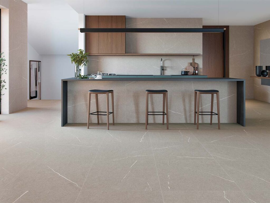 Suelo porcelánico Origins Grey efecto piedra con vetas blancas, instalado en el suelo y paredes de una cocina moderna con isla y muebles de madera