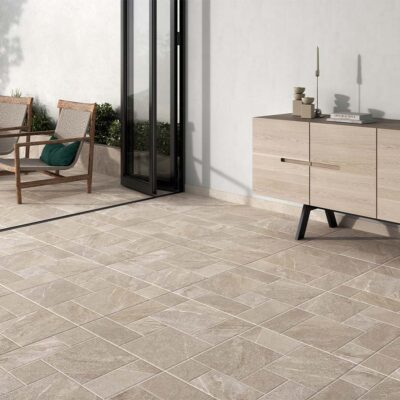 Suelo porcelánico rústico Sakhir multiformato en tono marfil, instalado en una terraza exterior con acceso a un interior moderno