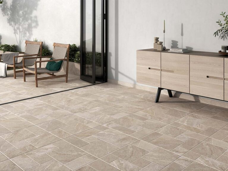 Suelo porcelánico rústico Sakhir multiformato en tono marfil, instalado en una terraza exterior con acceso a un interior moderno