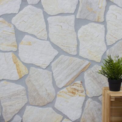 Revestimiento de pared porcelánico imitación piedra en tonos claros con juntas grises, decorado con planta en maceta.