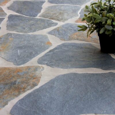 Revestimiento porcelánico gris y marrón en imitación piedra natural, instalado en un patio exterior con plantas decorativas.