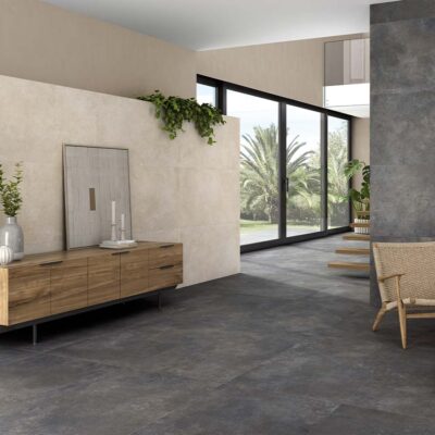 Pared de acento en un salón moderno revestida con el azulejo Feroe Greige, que aporta una textura de efecto piedra en tono greige claro, en contraste con el suelo y la chimenea oscuros.