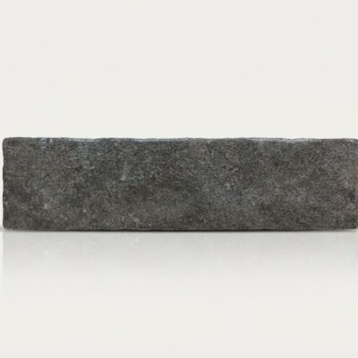 Baldosa de suelo porcelánico efecto piedra, textura rugosa y color gris oscuro intenso.