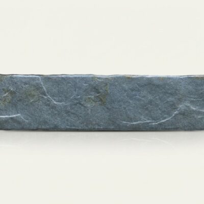 Baldosa rectangular de suelo porcelánico imitación piedra en tono azul grisáceo sobre fondo claro.