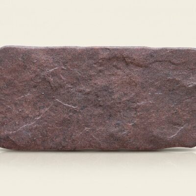 Baldosa cerámica efecto piedra rodeno con textura rústica y bordes irregulares.