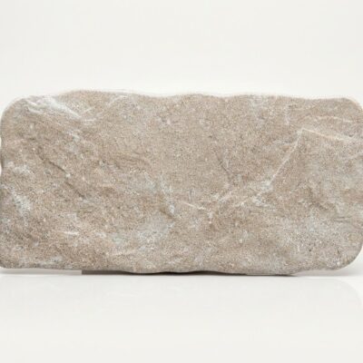 Baldosa porcelánica beige con textura de piedra country y bordes irregulares sobre fondo blanco.