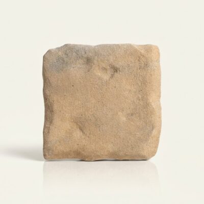 Una baldosa porcelánica tipo piedra Benisa teja de color arena con textura rugosa.