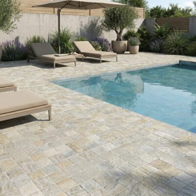 Piscina exterior con suelos porcelánicos rústicos efecto piedra en tonos claros.