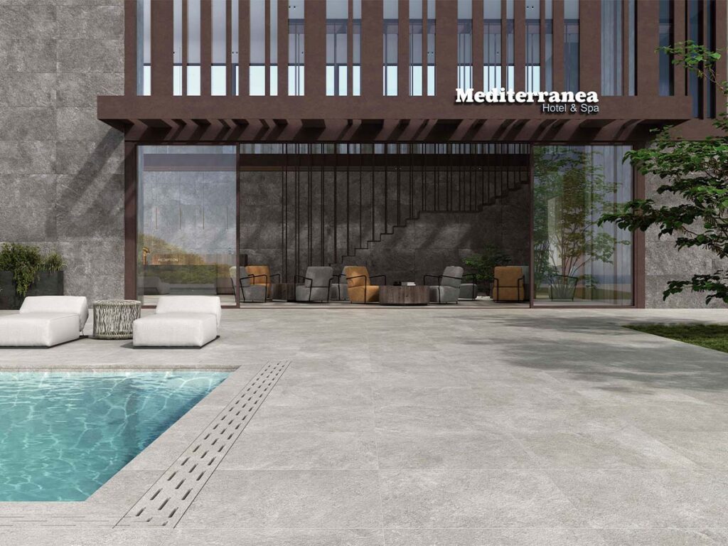 suelo porcelánico antideslizante exterior arenite grey en terraza con piscina de borde infinito y tumbonas blancas frente al mar