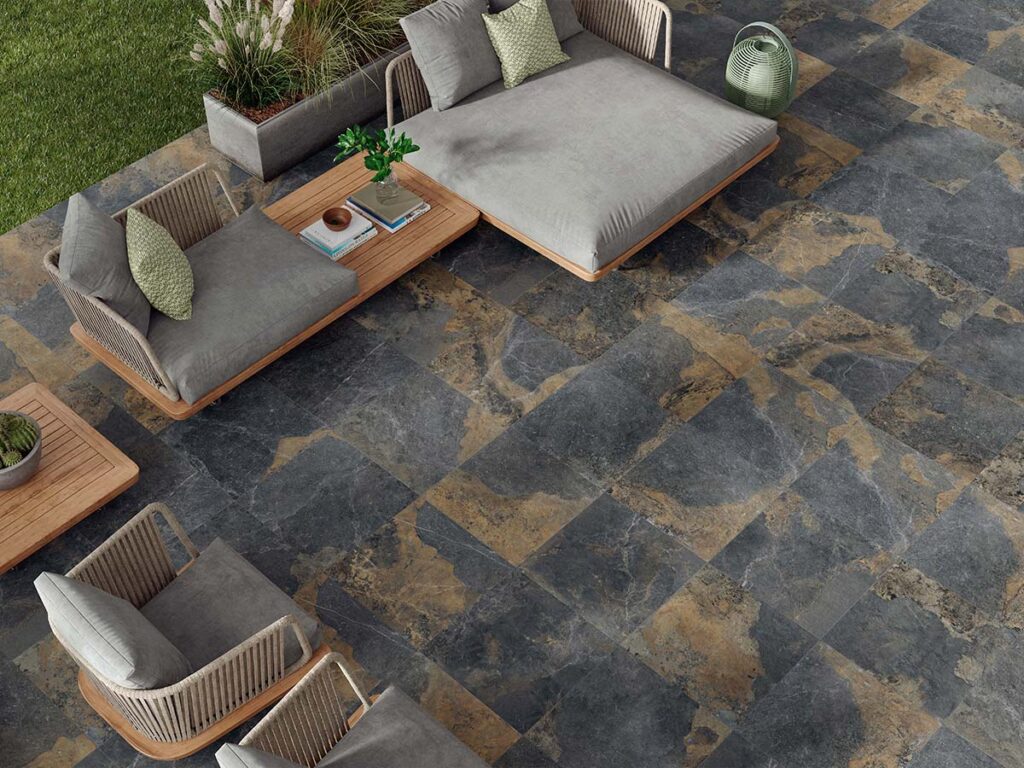 suelo porcelánico para exterior efecto piedra strato natural instalado en una amplia terraza con piscina infinita, tumbonas de diseño y una zona de comedor exterior bajo una estructura moderna, todo rodeado de un entorno natural