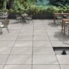 Suelo porcelánico para exterior Sakhir Grey, imitación piedra con vetas claras, instalado sobre plots o pedestales en una amplia terraza con mobiliario.