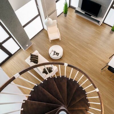 Vista aérea de un salón moderno con suelo porcelánico imitación madera rectificado leroy merlin, una escalera de caracol y grandes ventanales.