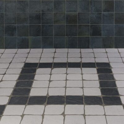 suelo de interior con azulejos cuadrados de imitación piedra que combinan blanco y gris oscuro en un patrón geométrico sobre una pared de azulejos oscuros