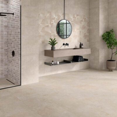 Suelo de un baño moderno pavimentado con porcelánico antideslizante Feroe Greige, que sirve de base neutra para las paredes decorativas con mosaicos y patrones geométricos.