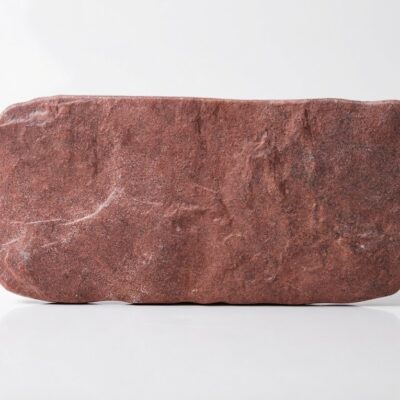 Muestra de suelo porcelánico efecto piedra rodeno con textura rugosa y tono rojizo.