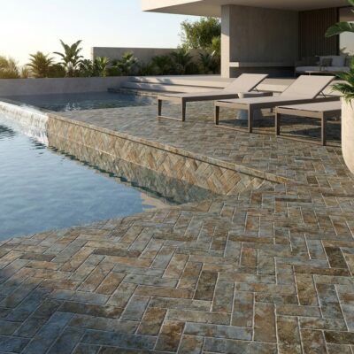 Suelo porcelánico en patrón espiga rodeando una piscina moderna con tumbonas.