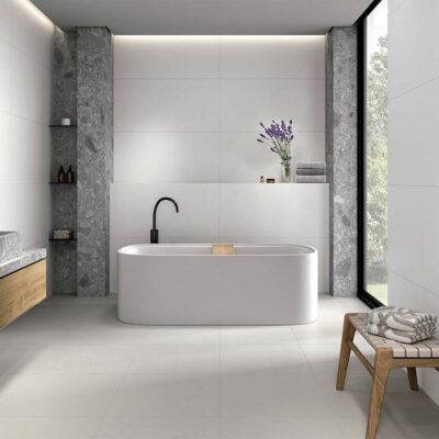 Baño moderno con suelo porcelánico antideslizante en tono blanco y revestimiento cerámico liso, combinado con detalles en piedra natural gris.
