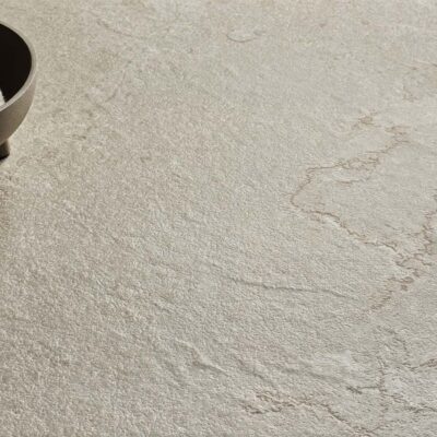 Textura de suelo porcelánico antideslizante con acabado efecto piedra natural en tono beige grisáceo, ideal para exteriores.