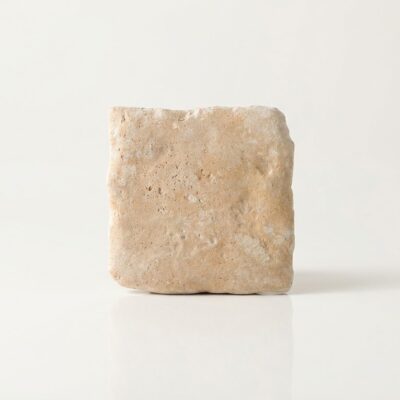 Una baldosa cerámica porcelánica beige con textura rugosa de imitación piedra sílex.