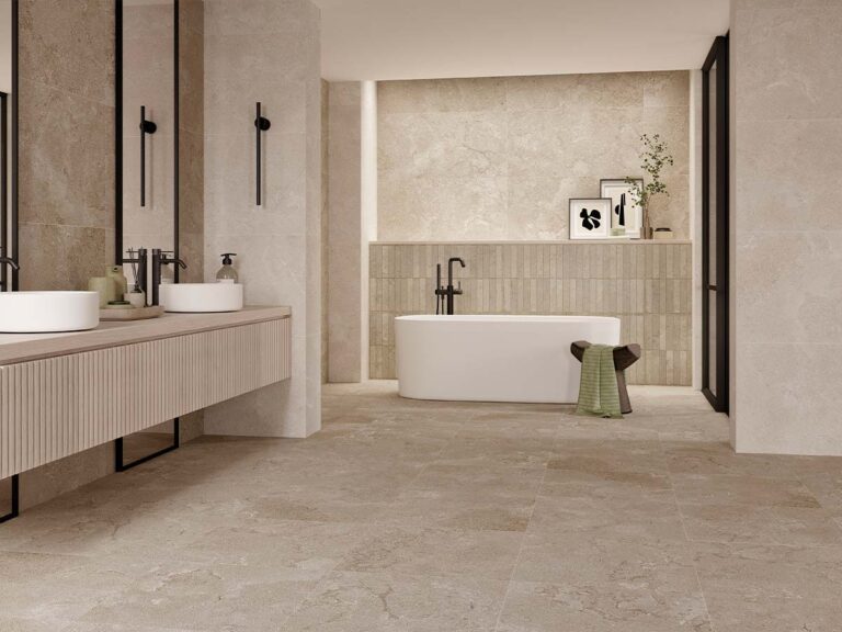 Baño moderno con suelo de gres porcelánico beige efecto piedra natural, revestimiento cerámico decorativo y bañera exenta de diseño minimalista.