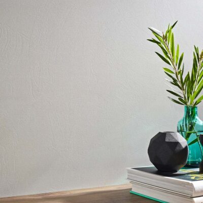 Revestimiento cerámico blanco mate con textura sutil en pared interior, decorado con objetos sobre superficie de madera.