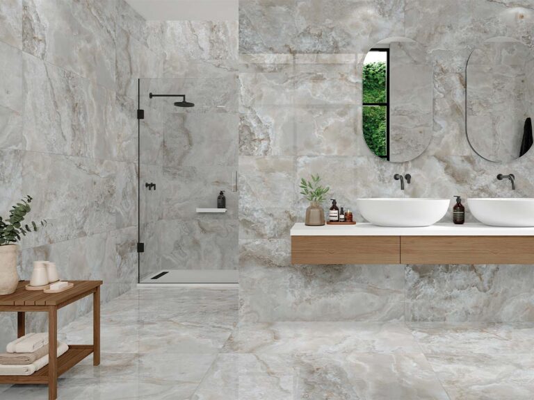 Baño moderno revestido con porcelánico efecto ónix gris beige, con ducha de cristal, doble lavabo sobre mueble flotante y detalles decorativos