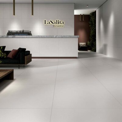 Zona lounge con suelo porcelánico gran formato en tono blanco mate y revestimiento cerámico liso, ideal para espacios comerciales modernos.