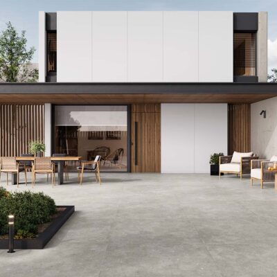 Terraza moderna con pavimento porcelánico gris efecto cemento, mobiliario exterior de madera y fibra, y fachada minimalista con paneles blancos y detalles en madera